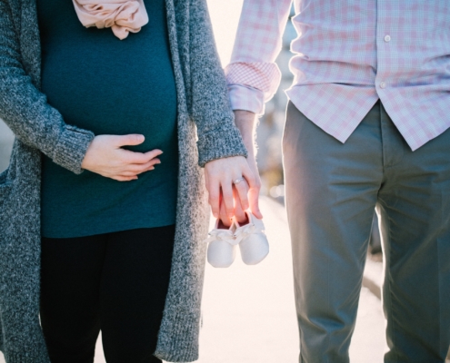 man standing beside pregnant woman holding baby's shoes during daytime